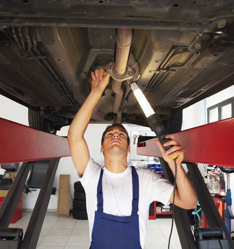 Mechanic standing under car engine and holding lamp - Class 4, 5 & 7 MOT Testing